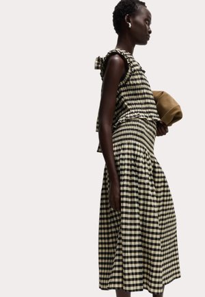 Vestido a cuadros en negro y crema con detalle de hombros con volantes, cintura fruncida y falda acampanada. Acompañado de un clutch beige.
