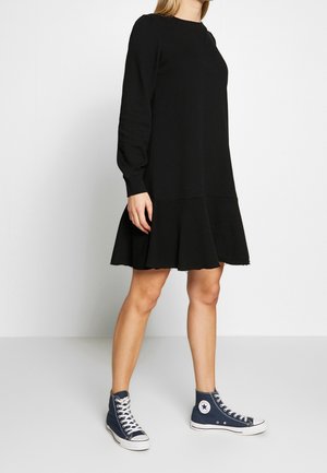 Schwarzes Langarmkleid mit schwingendem Saum, Rundhalsausschnitt und weichem Material, kombiniert mit blauen hochgeschnittenen Turnschuhen.