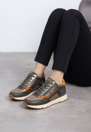 Zapatillas deportivas con una mezcla de materiales marrones, verdes y naranjas; presentan una parte superior texturizada, cordones y detalle de cremallera lateral; suela blanca.