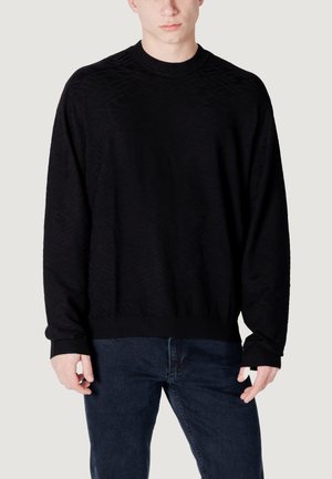 Zwarte gebreide trui met een gestructureerd ruitpatroon, voorzien van een ronde hals en ribgebreide boorden en zoom, gedragen met donkere jeans.