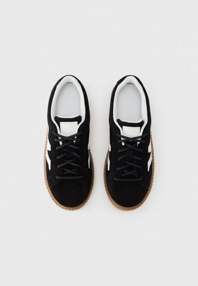 Μαύρα σουέντ αθλητικά παπούτσια με λευκές λεπτομέρειες, κλείσιμο με κορδόνια και υφασμένο καφέ λαστιχένιο πέλμα. Στρογγυλερή μύτη και ενίσχυση στο κολάρο.