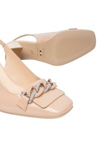 Scarpe slingback in pelle verniciata color nude con punta quadrata, tacco piatto e un accento decorativo in catena su una suola texturizzata.