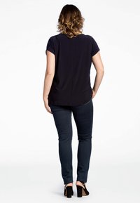 Dunkelblaues, kurzärmliges Oberteil mit rundem Ausschnitt und lässiger Passform, kombiniert mit dunkelblauen Jeans und schwarzen, hohen Sandalen. Glatte Stofftextur.