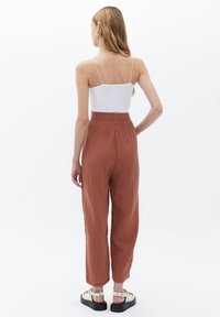 Rustinvärdiga, strukturerade vida byxor med elastisk midja, i kombination med en vit kroppsnära linne och svarta sandaler med gulddetaljer.