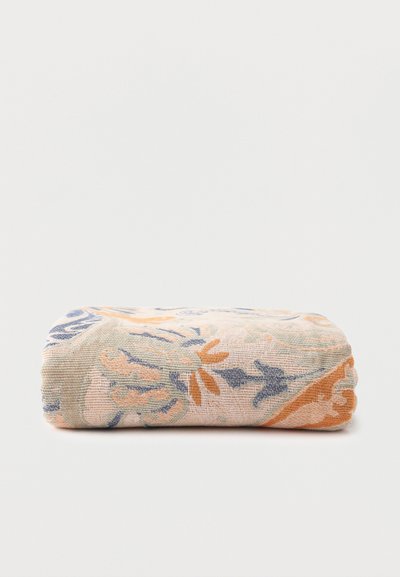 Tissu beige plié avec des motifs floraux et abstraits bleus et orange sur un fond uni clair.