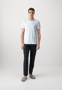 T-shirt en coton bleu clair, pantalon de pyjama à carreaux noirs et chaussons en feutre gris. Le T-shirt a un col rond ; le pantalon présente un motif à carreaux.