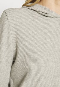 Grauer gerippter Hoodie mit lockerer Passform, bestehend aus einem strukturierten Stoff und einer angenähten Kapuze, die vertikale Rippungen auf der Oberfläche zeigt.