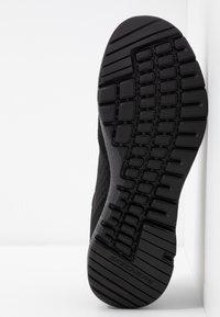 Svart Skechers-sula med texturerat mönster och varumärke, vinklad mot en vit bakgrund.