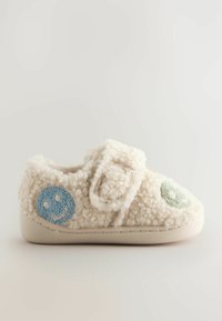 Chausson moelleux de couleur crème avec une sangle en Velcro, décoré d'appliqués souriants bleus et verts sur les côtés, et d'une semelle en caoutchouc beige.