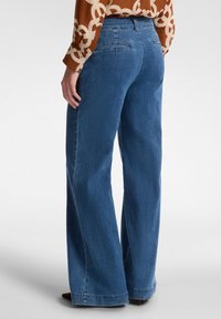 Jeans de mezclilla azul de pierna ancha con una cintura alta, que cuentan con dos bolsillos traseros y una textura suave. Acabados con un dobladillo recto.