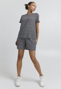 Ensemble imprimé floral noir et blanc comprenant un haut à manches courtes et un short assorti en tissu léger. Des baskets blanches complètent le look.