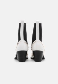 Botas de tobillo en blanco y negro con un acabado texturizado, que cuentan con un tacón cuadrado y tachuelas de cobre a lo largo de las costuras. Paneles elásticos verticales.