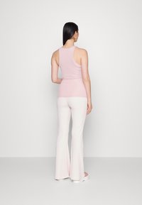 Top sem mangas de um rosa claro com um design ajustado, combinado com calças de boca larga, também em rosa claro. Tecido suave com uma textura subtil.