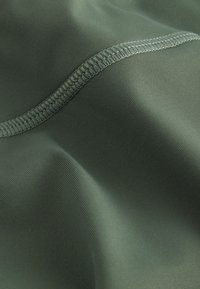 Nahaufnahme eines grünen Stoffes mit detaillierter, doppelt genähter Naht und glatter Textur mit leichten Falten.