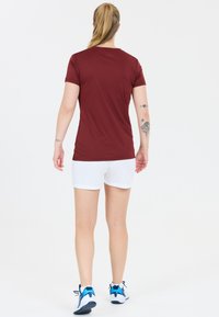 Bordeaux kortærmet skjorte, hvide shorts, blå og sorte sneakers. Tatovering på armen. Enkel design, tætsiddende, glat tekstur.