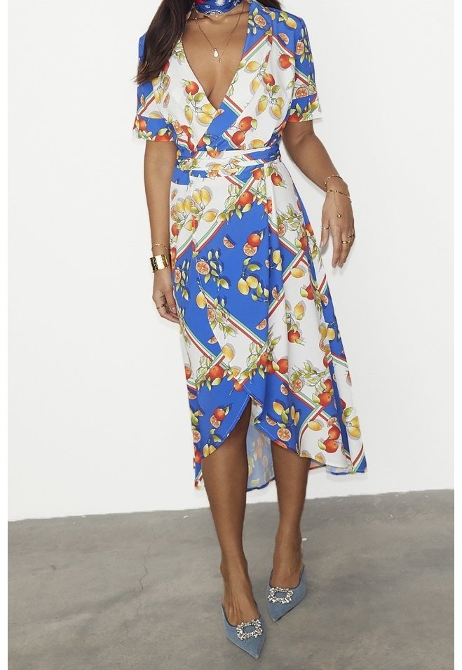 Robe portefeuille à fleurs dans des tons de bleu, blanc et vert. Manches courtes, décolleté en V, et ourlet au niveau du genou avec une coupe diagonale. Assortie à des talons bleus.