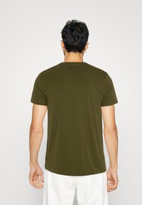 Oliven grøn T-shirt med korte ærmer i blødt stof, med rund halsudskæring og afrundet kant, der har et diskret logo nær bunden til venstre.