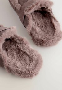 Flauschige, mauvefarbene Hausschuhe mit einem plüschigen, weichen Innenfutter und einem Riemen oben für einen sicheren Sitz. Die strukturierte Außenseite sorgt für visuelles Interesse.