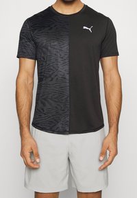 Camiseta deportiva negra con un patrón de cebra texturizado en una mitad. Presenta un cuello redondo y el logo blanco de Puma en el pecho.