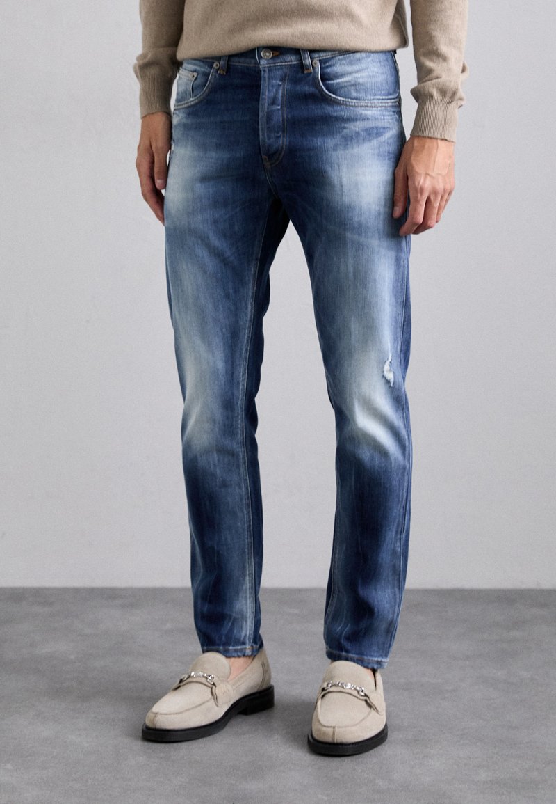 Jeans in denim blu sbiadito con vestibilità slim, caratterizzati da leggere pieghe, ginocchia strappate e classico design a cinque tasche.