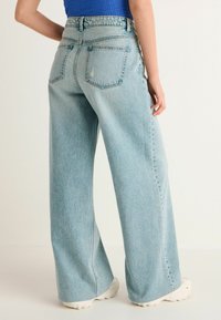 Svetlomodré vysoké široké džínsy majú textúrovaný denimový povrch, dve zadné vrecká a jemné vyšívané detaily.