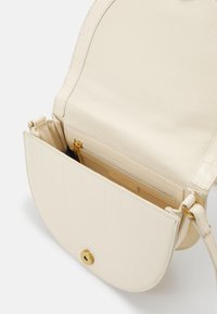 Borsa a tracolla di colore crema con una patta curva, hardware dorato e una tasca interna con zip. Realizzata in materiale sintetico con una finitura liscia.