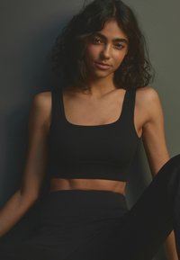 Crni rebrasti crop top s četvrtastim izrezom, s širokim trakama i prilagođenim dizajnom, uparen s crnim tajicama visokog struka.