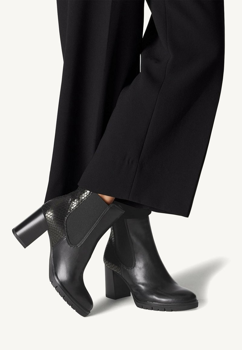 Bottes courtes noires à talons avec une finition en cuir lisse, des panneaux latéraux élastiques et des accents texturés ressemblant à de la peau de serpent sur le talon.