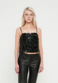 Top nero in paillettes con spalline sottili, design corto e texture liscia. Abbinato a pantaloni aderenti in pelle nera.