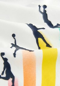 Textil s basketbalovou tematikou na bílém pozadí, s tmavými siluetami hráčů a barevnými vertikálními pruhy v žluté, oranžové a zelené barvě.