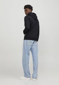 Sudadera negra con capucha, textura suave, combinada con unos vaqueros sueltos de color azul claro y zapatillas blancas, vista desde atrás.