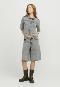 Camisa de mezclilla gris cortada con mangas cortas y cierre de botones, combinada con pantalones cortos de mezclilla gris hasta la rodilla, complementada con botas de tobillo marrones.