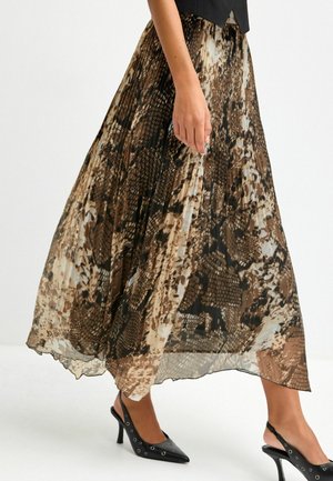 Femme portant une jupe plissée marron et noire à motif peau de serpent avec des chaussures à talons hauts noires à bride arrière, marchant sur fond blanc.