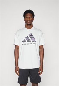 Hvid t-shirt med korte ærmer med et lilla- og sort grafisk design med teksten "BASKETBALL", der er parret med sorte træningsshorts.