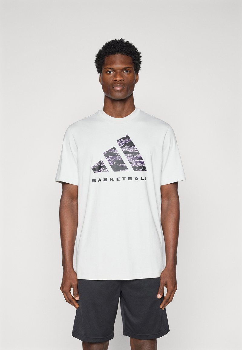 Hvid t-shirt med korte ærmer med et lilla- og sort grafisk design med teksten "BASKETBALL", der er parret med sorte træningsshorts.
