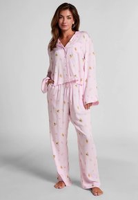 Roze pyjama set gemaakt van zacht stof, bestaande uit een knoopsluitend bovenstuk met lange mouwen en een broek met elastische taille, versierd met bloemmotieven.