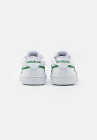 Bílé tenisky s zelenými akcenty, hladký kožený svršek, polstrovaný límec, strukturovaná gumová podrážka a logo Reebok na patě a boku.