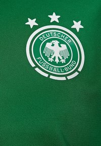 Maillot de sport vert avec un logo circulaire blanc représentant un aigle, le texte "Deutscher Fussball-Bund" et trois étoiles blanches au-dessus.
