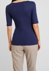 Marinblå kortärmad topp med båtkrage, mjukt tyg och en figurnära design. Kombinerad med rutiga beige och bruna löst sittande byxor.