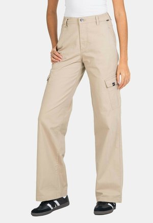 Beige cargo pants made of fabric, featuring a relaxed fit, side pockets, and a zip fly with a button closure. Worn with black sneakers.