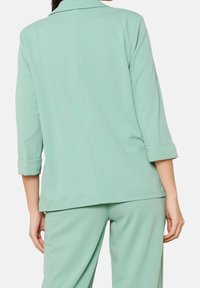 Miętowy blezer o dopasowanym kroju, z podwiniętymi rękawami, gładką teksturą i prostym krojem z tyłu, w zestawie z pasującymi spodniami.