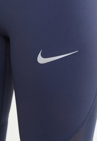 Marina sportleggings tillverkade av elastisk tyg, med en silverfärgad Nike-svishlogotyp på låret och en slät, sömlös konstruktion.