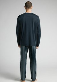 Marineblaues Langarmshirt mit lockerer Passform, kombiniert mit blau-grün gestreiften Schlafanzughosen, die einen elastischen Bund und einen geraden Schnitt haben.