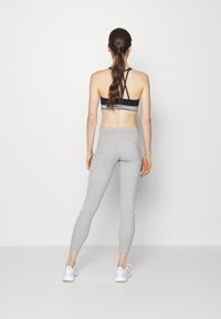 Grå leggings med en figursydd design och sidogylfar, kombinerat med en svart sport-bh med korsade band på baksidan och horisontella ränder.