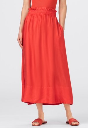Femme portant une jupe rouge taille haute, longueur cheville avec des poches, un top rouge sans manches assorti et des sandales plates rouges à enfiler.