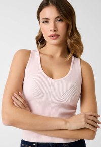 Débardeur rose clair côtelé avec un col en V, présentant des rayures verticales texturées et des motifs chevrons subtils. Tissu doux et ajusté.