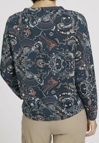 Maglietta a maniche lunghe con uno sfondo blu scuro decorato da motivi floreali e astratti multicolori. Tessuto morbido.