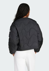 Černá péřová bunda s vlnitým prošíváním, zkrácený střih a hladká textilie. Na levém rukávu se nachází logo.