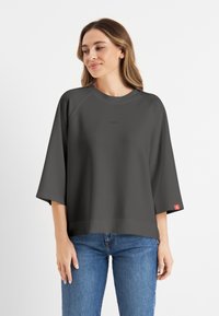 Donkergrijze oversized t-shirt met een ronde halslijn en raglan mouwen. Bevat een subtiele logo aan de voorkant en een rode label op de mouw.