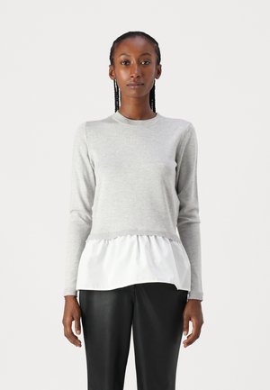 Grijze gebreide pullover met lange mouwen, voorzien van een witte gelaagde ruches onderkant en geribde manchetten, gecombineerd met zwarte pantalons.